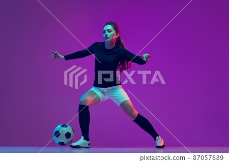 Professional female soccer player dribbling football ball isolated on purple studio background in neon light. Sport, action, motion, fitness Professional female soccer player dribbling football ball isolated on purple studio background in neon light. Sport, action, motion, fitness 87057889