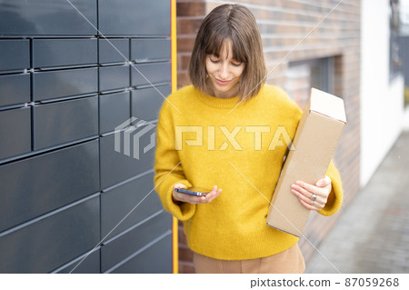 Happy woman with parcel and phone standing near automatic post terminal Happy woman with parcel and phone standing near automatic post terminal 87059268