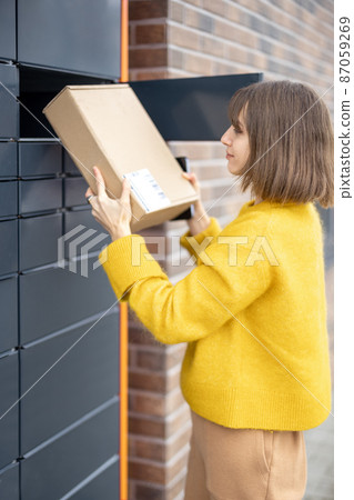 Woman getting parcel from cell of automatic post terminal outdoors Woman getting parcel from cell of automatic post terminal outdoors 87059269