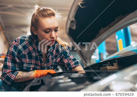 Car reapir. Young red-headed girl, auto mechanic working at auto service station using different work tools. Gender equality. Work, occupation, car Car reapir. Young red-headed girl, auto mechanic working at auto service station using different work tools. Gender equality. Work, occupation, car 87059420