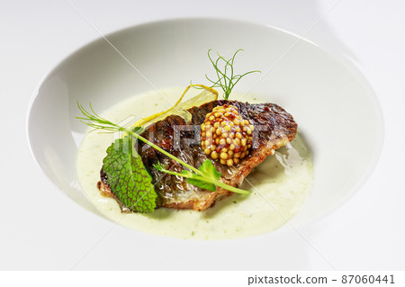 Grilled fish fillet with sauce, mustard and herbs on a white plate. Close-up. Restaurant serving. Seafood photo 87060441