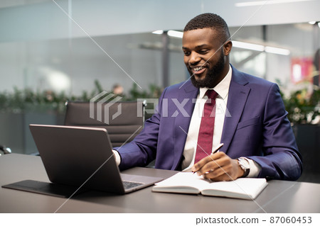 Happy black businessman using laptop and taking notes Happy black businessman using laptop and taking notes 87060453