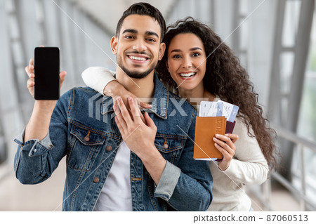 Best Booking App. Arab Couple Holding Passports With Tickets And Blank Smartphone Best Booking App. Arab Couple Holding Passports With Tickets And Blank Smartphone 87060513