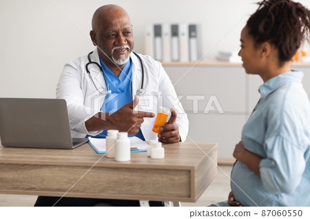 Mature experienced black doctor showing pills to pregnant lady Mature experienced black doctor showing pills to pregnant lady 87060550