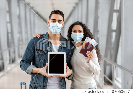 Middle Eastern Couple In Medical Masks Showing Blank Digital Tablet At Airport Middle Eastern Couple In Medical Masks Showing Blank Digital Tablet At Airport 87060667