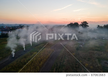 Aerial view of agricultural waste bonfires from dry grass and straw stubble burning with thick smoke polluting air during dry season on farmlands causing global warming and carcinogen fumes 87061663