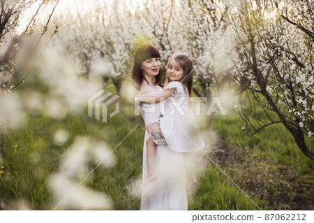 Mother holding daughter under branches of blooming trees 87062212