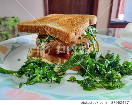 burger patty between two pieces of bread, sauce dripping with condiments. 87062487