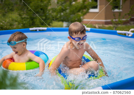Two boys brothers in the outdoor outdoor pool near the house swim and play. Colored, swimming, bright, rainbow circles. 87062560