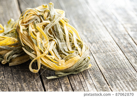 Egg pasta. Noodles nest with spinach flavor on wooden table. 87062870