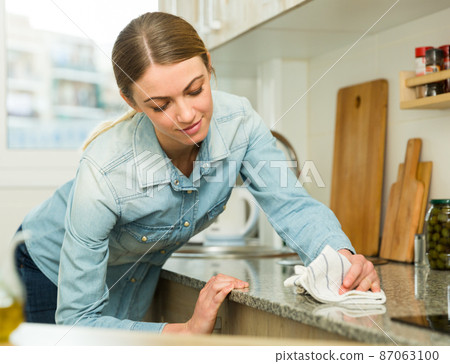 Smiling woman is cleaning surface on the kitchen at the home 87063100
