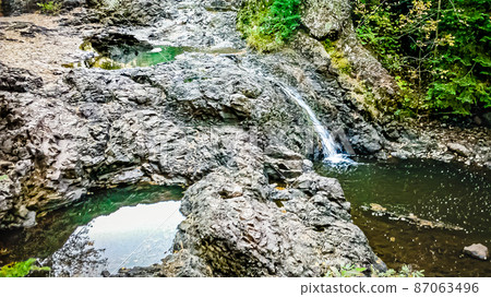 A small and cute waterfall flowing through the rocks A small and cute waterfall flowing through the rocks 87063496
