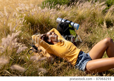 Relaxed biracial woman laying with eyes closed on meadow on a sunny day Relaxed biracial woman laying with eyes closed on meadow on a sunny day 87068293