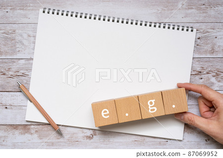 Building blocks, notebooks, pens, human hands with "e.g." written on them 87069952