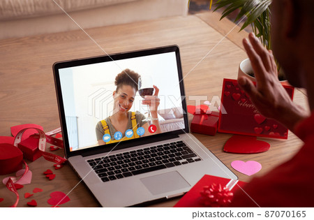 Smiling biracial young woman with red wine during online dating with boyfriend on valentine day Smiling biracial young woman with red wine during online dating with boyfriend on valentine day 87070165