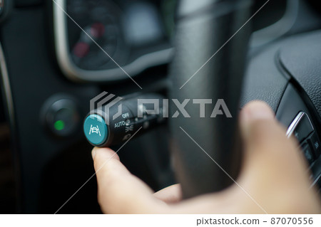 Unrecognizable man driver activating the adaptive cruise control or steering assistant on the control stick behind steering wheel in electric vehicle - EV. Driving Assist system in modern car. Unrecognizable man driver activating the adaptive cruise control or steering assistant on the control stick behind steering wheel in electric vehicle - EV. Driving Assist system in modern car. 87070556