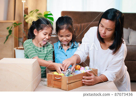 Asian mother and her daughters are playing with baby bunny and decorating easter eggs preparing for Easter at home. Happy family Happy easter Happy holiday. Asian mother and her daughters are playing with baby bunny and decorating easter eggs preparing for Easter at home. Happy family Happy easter Happy holiday. 87073436