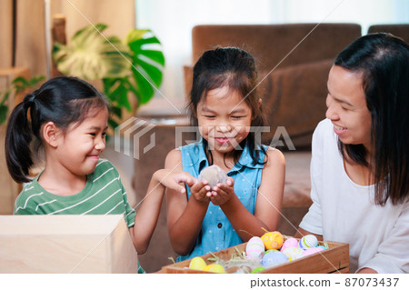 Asian mother and her daughters are playing with baby bunny and decorating easter eggs preparing for Easter at home. Happy family Happy easter Happy holiday. Asian mother and her daughters are playing with baby bunny and decorating easter eggs preparing for Easter at home. Happy family Happy easter Happy holiday. 87073437