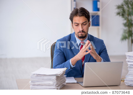 Young male employee and too much work in the office Young male employee and too much work in the office 87073648