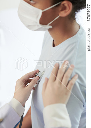 Close-up of doctor examining the heartbeat of patient in mask with stethoscope during her visit at hospital 87075077