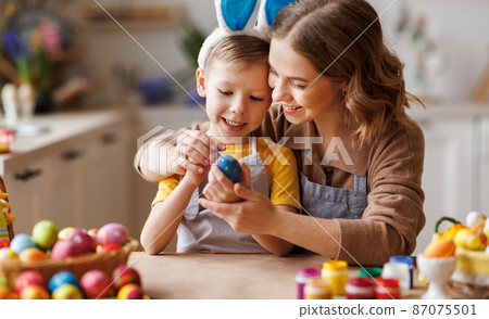 Loving young mother teaching happy little kid son to decorate Easter eggs while sitting in kitchen Loving young mother teaching happy little kid son to decorate Easter eggs while sitting in kitchen 87075501
