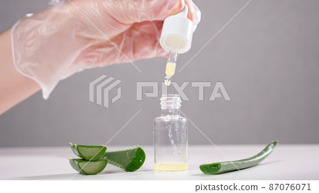 Specialist drops aloe juice into glass bottle on white table 87076071