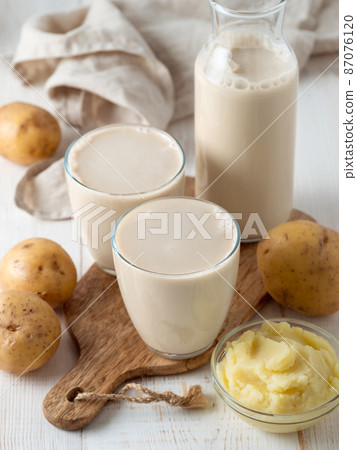 Potato milk pouring into glass on white wooden bg 87076120