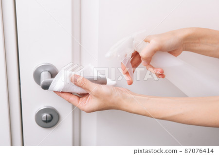 Cleaning white door handles with an antiseptic wet wipe and sanitizer spray. Disinfection in hospital and public spaces against corona virus. Woman hand using towel for cleaning home room door link. Cleaning white door handles with an antiseptic wet wipe and sanitizer spray. Disinfection in hospital and public spaces against corona virus. Woman hand using towel for cleaning home room door link. 87076414