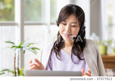 一位在室內戴耳機並前往筆記本電腦的女商人 一位在室內戴耳機並前往筆記本電腦的女商人 87077621