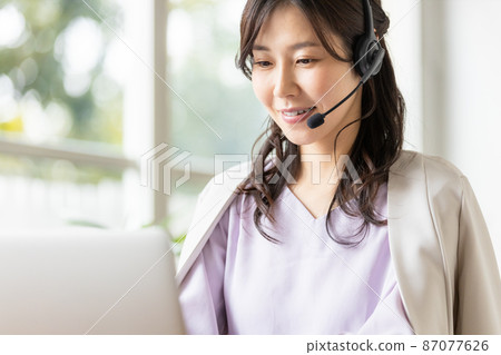 一位在室內戴耳機並前往筆記本電腦的女商人 87077626