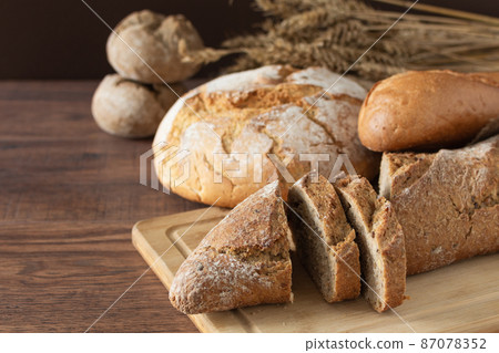 Loaf of bread sliced and other variety of bread on wooden table. 87078352