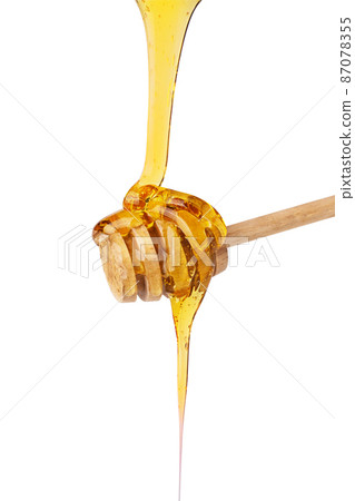 Honey dripping on wooden honey dipper isolated on white background. Organic honey drop. 87078355