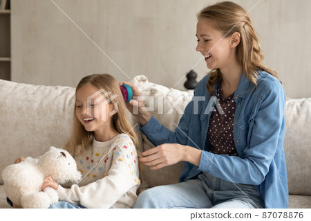 Happy loving mom combing long hair of adorable preschool daughter Happy loving mom combing long hair of adorable preschool daughter 87078876