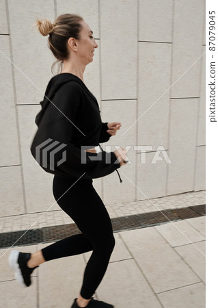 A woman in a black tracksuit does sports in the park 87079045