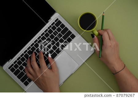 Female designer holing coffee cup and using computer laptop over green background. 87079267