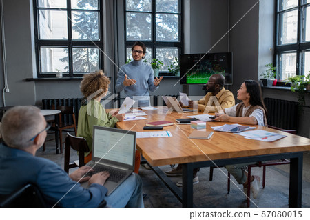 Young confident business coach making presentation in front of audience Young confident business coach making presentation in front of audience 87080015