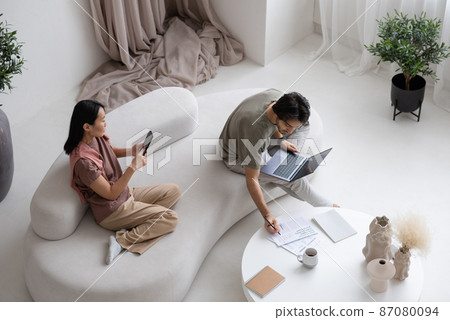 Young man making notes in document while female texting in mobile phone Young man making notes in document while female texting in mobile phone 87080094