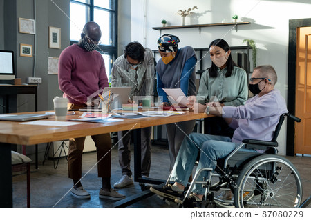 Mature man in wheelchair and his Asian colleague discussing document 87080229