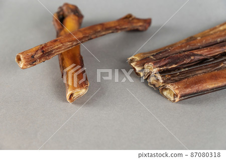 Pet chew treats. Natural dried dog treats against a gray background. Group of bully sticks. Pet supplies. Pet chew treats. Natural dried dog treats against a gray background. Group of bully sticks. Pet supplies. 87080318