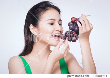 Young beautiful asian woman eating fresh grapes isolated on white background 87080931