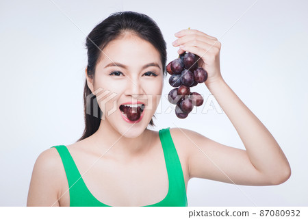 Young beautiful asian woman eating fresh grapes isolated on white background 87080932