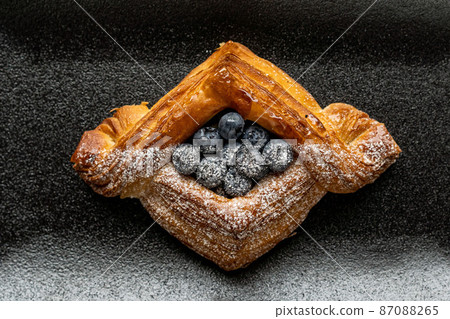dessert is a small puff pastry pie with stuffing inside on a black serving plate on a black background . A piece of cake with a cut 87088265