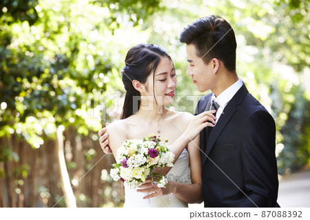 young asian groom kissing bride outdoors during wedding ceremony young asian groom kissing bride outdoors during wedding ceremony 87088392