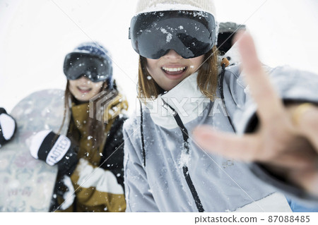 Snowboarding girls posing at a snowy ski resort Snowboarding girls posing at a snowy ski resort 87088485