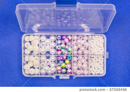 Transparent plastic container with beads and beads of different sizes, blue background 87088486