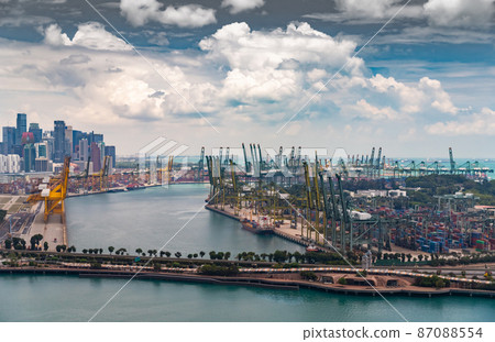 The huge busiest logistic port in Singapore, plenty of cranes to move containers, huge cargo ships in the background, skyscrapers on background The huge busiest logistic port in Singapore, plenty of cranes to move containers, huge cargo ships in the background, skyscrapers on background 87088554