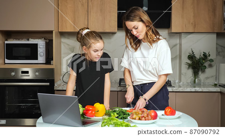 Mother and teen daughter watch recipe of salad in laptop 87090792