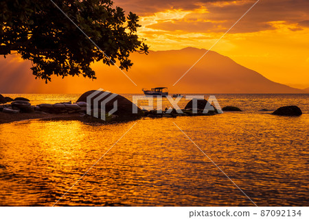 Warm sunset on beach and quiet ocean with boat in Florianopolis Warm sunset on beach and quiet ocean with boat in Florianopolis 87092134