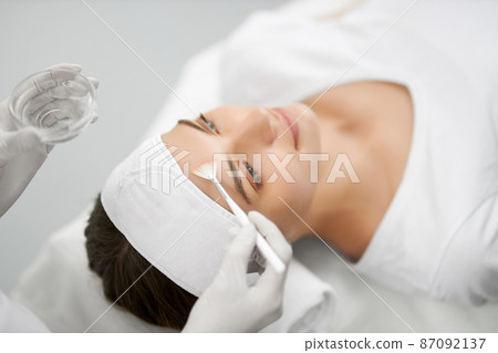Side view of beautician holding brush and doing cleaning face for young beautiful woman. Concept of procedure for rejuvenation skin or improvements in professional beauty salon. Side view of beautician holding brush and doing cleaning face for young beautiful woman. Concept of procedure for rejuvenation skin or improvements in professional beauty salon. 87092137
