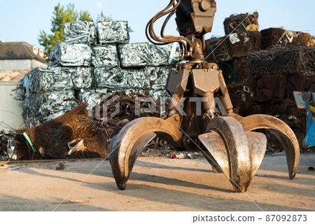 Large tracked excavator working a steel pile at a metal recycle yard. Industrial scrap metal recycling - selective focus, copy space Large tracked excavator working a steel pile at a metal recycle yard. Industrial scrap metal recycling - selective focus, copy space 87092873